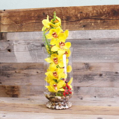 tall glass vase filled with yellow orchids and red berries