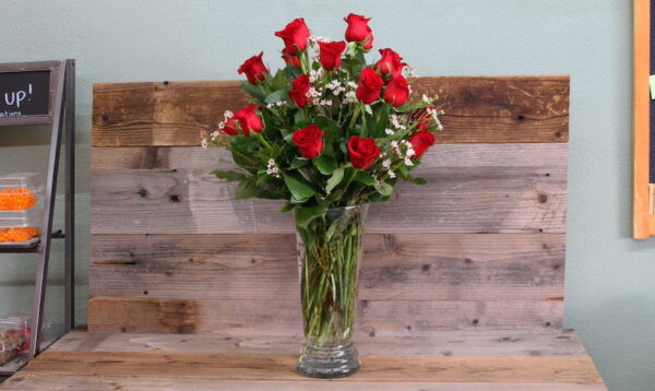 two dozen red roses in a glass vase on a table.