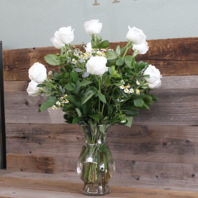 one dozen white roses and greens in a clear, glass vase.