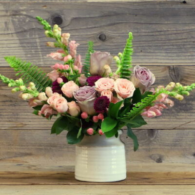 small bouquet of pastel flowers and greens in a white vase.