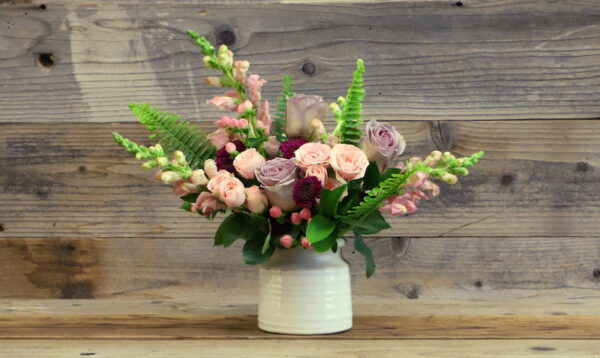 small bouquet of pastel flowers and greens in a white vase.