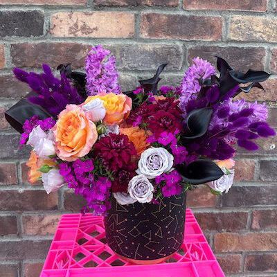 large arrangement of flowers in a black vase sitting on a pink crate