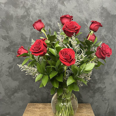 twelve red roses and greenery in a glass vase sitting on a table