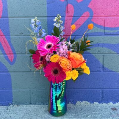 bright, colorful flower bouquet in a glossy vase sitting in front of a mural wall