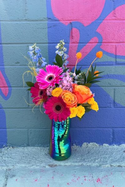 bright, colorful flower bouquet in a glossy vase sitting in front of a mural wall