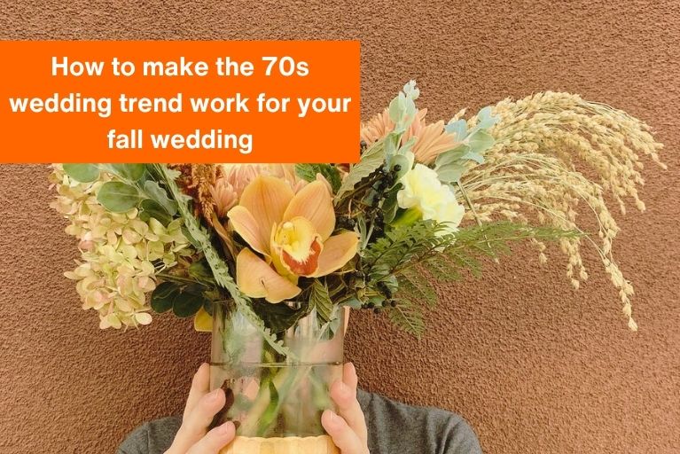 person holding a vase filled with peach toned flowers and greenery with the text "How to make the 70s wedding trend work for your fall wedding" in the foreground