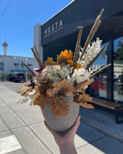 outstretched hand holding a small vase of autumn flowers at a coffee shop